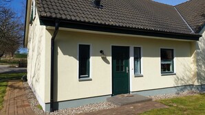 Uma casa térrea com porta verde, duas janelas e telhado de telhas.