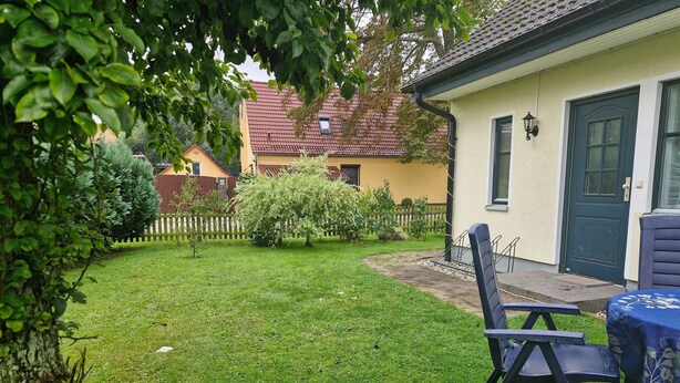 Um jardim bem cuidado com gramado, cerca de madeira e uma casa com porta e janelas escuras.