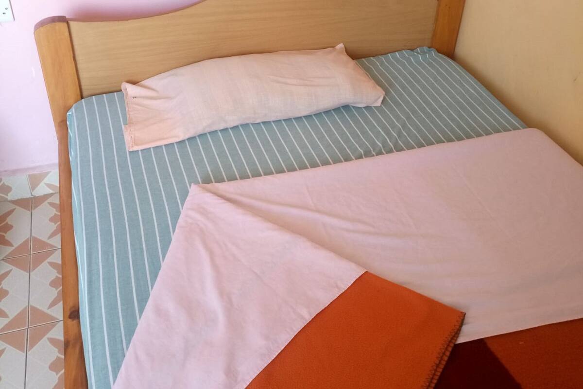 Uma cama de solteiro com cabeceira de madeira, colcha azul e branca listrada, travesseiro branco e manta laranja dobrada.