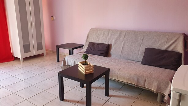Una sala de estar con un sofá, dos mesitas auxiliares, una pequeña mesa de madera con una planta y una cortina roja.
