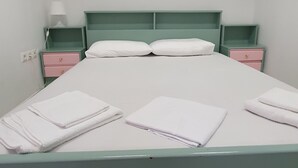 Una cama bien hecha con sábanas y almohadas blancas, dos mesitas de noche con lámparas, y un mueble cajonera rosa.