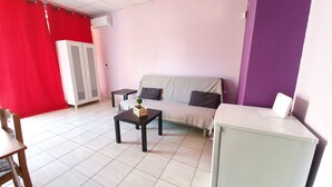 Una habitación con sofá, una mesita con planta, un armario y una cortina roja.