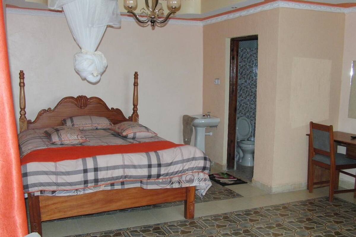 A bedroom with a wooden bed, a bedside table, a chair, a small sink, and a toilet.