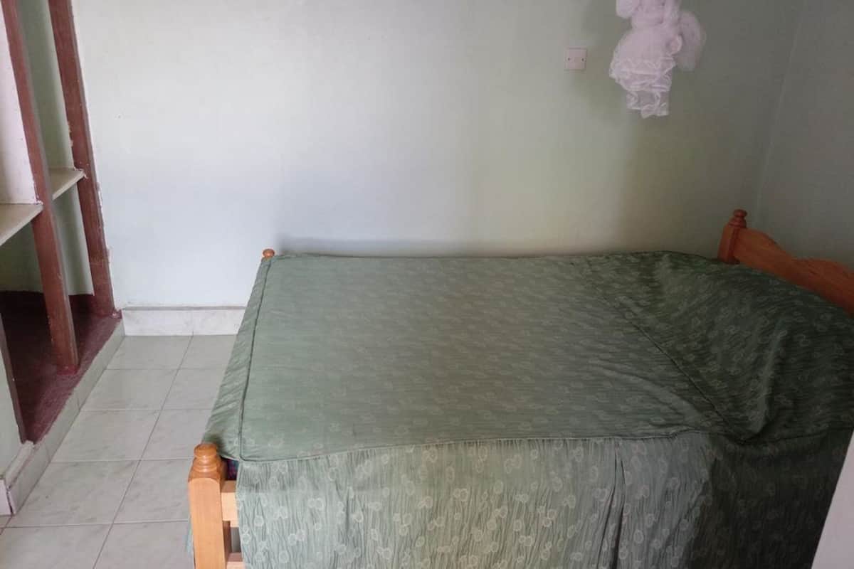 A single bed with a green bedspread in a room with white walls and a tiled floor.