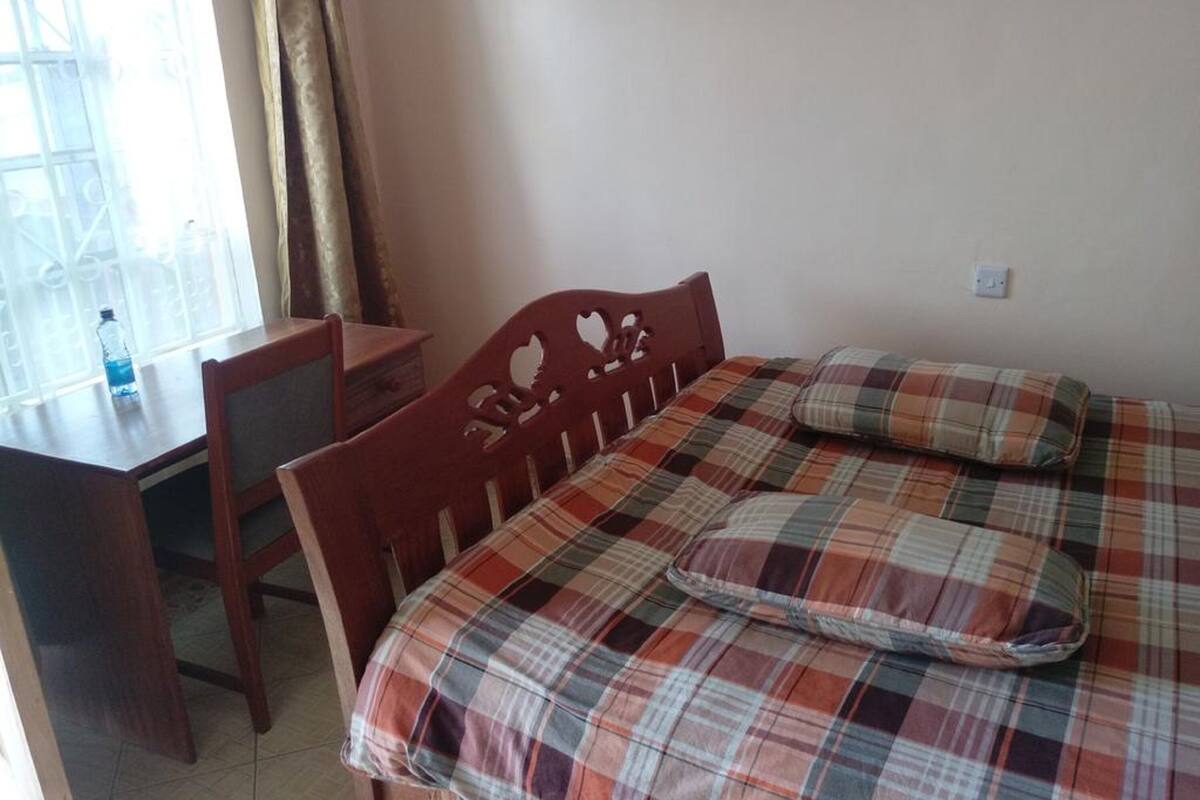 A room with a bed, a wooden headboard, a small table, and a window with curtains.