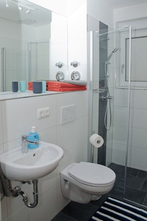 A modern bathroom with a white sink, toilet, and glass shower enclosure. - Die Villa Kreisel (Dresden)