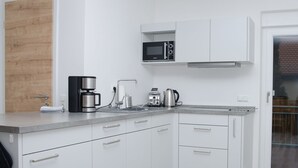 Une cuisine moderne avec des meubles blancs, un four à micro-ondes encastré, une machine à café et une bouilloire.