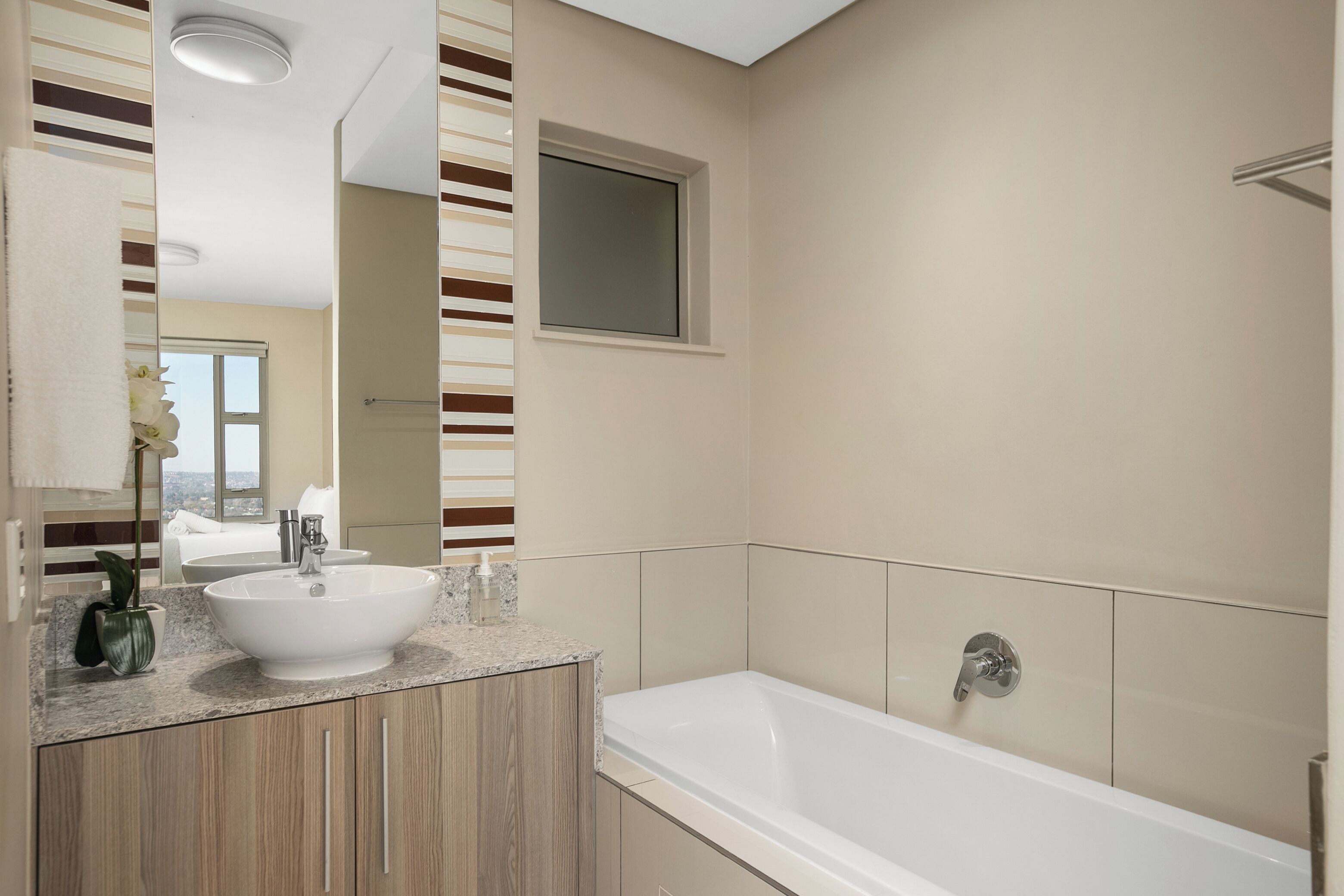Une salle de bain moderne avec une grande baignoire, un lavabo doté d’un plan de toilette en marbre et une fenêtre située au-dessus du miroir.