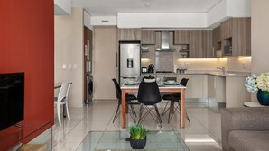 Une cuisine moderne avec un coin repas, un téléviseur et une table en verre agrémentée d’une plante.