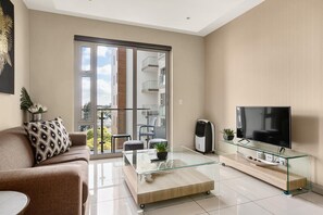 A modern living room with a glass coffee table, a sofa with patterned cushions, a flat-screen TV on a glass TV stand, and a view of a balcony with a building in the background. - Easy Stay - The Tyrwhitt (Johannesburg)