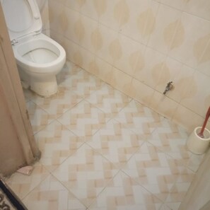 A bathroom with a toilet, patterned tiles, and a mop. - Harvester Restaurant (Nakuru)