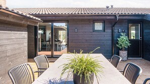 En terrasse med et langt bord og stole, en potteplante og et træterrasse.