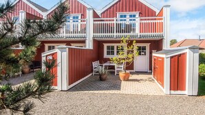 A two-story house with a red exterior and white trim, featuring a balcony and a paved driveway. - 5 Star Holiday Home in Blavand (Blavand)