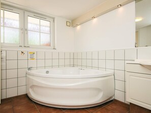 A bathroom with a large bathtub, white tiles, a window, and a sink.