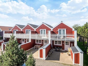 Række røde bygninger med hvide gelændere, en overdækket terrasse og udendørs siddepladser.