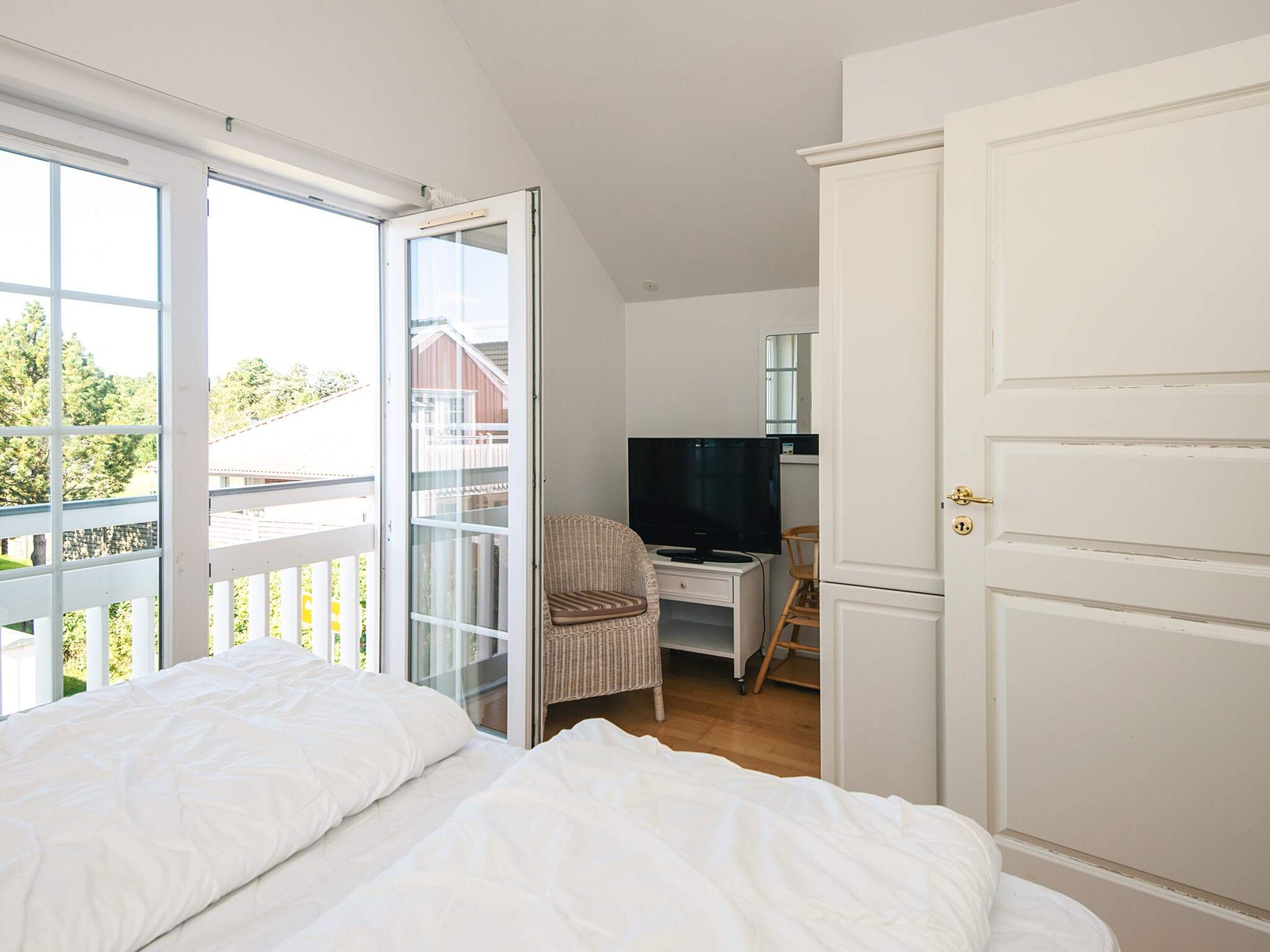 Une chambre à coucher comprenant un lit, un bureau avec une télévision et une porte-fenêtre coulissante donnant sur un balcon.