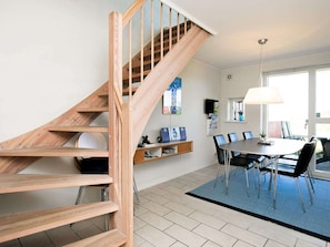 Ein modernes Interieur mit einer Holztreppe, einem Essbereich mit Tisch und Stühlen sowie einem an der Wand befestigten Fernseher.