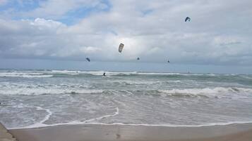 En strand med bølger, en klippe og drager på himlen.