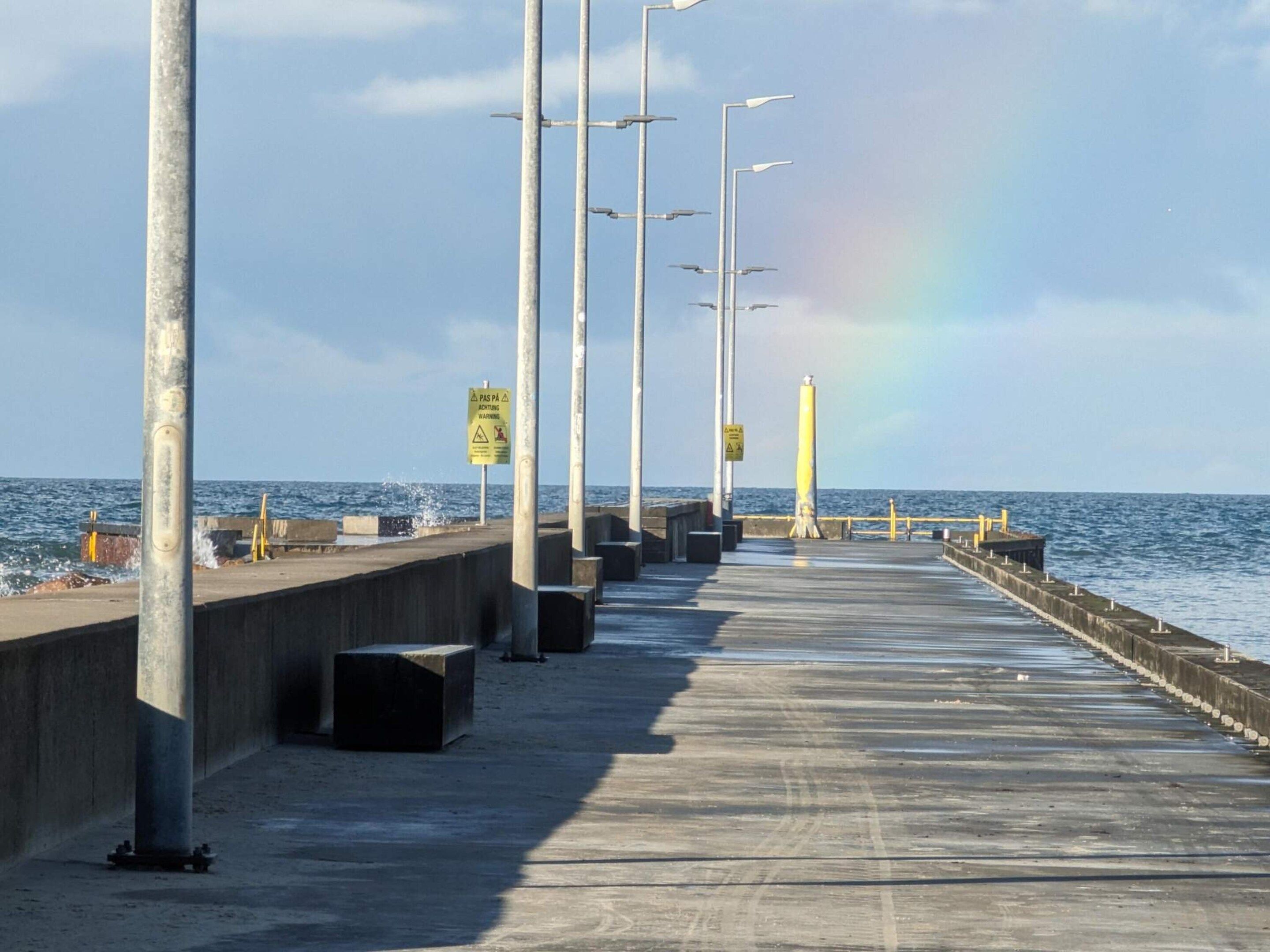 Une jetée dotée de lampadaires et de panneaux d’avertissement, qui mène à la mer.