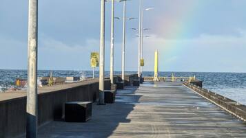 A pier with street lamps and warning signs, leading to the sea.