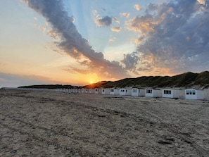 A row of white beach huts with a sunset in the background. - 5 Star Holiday Home in Lokken (Lokken)