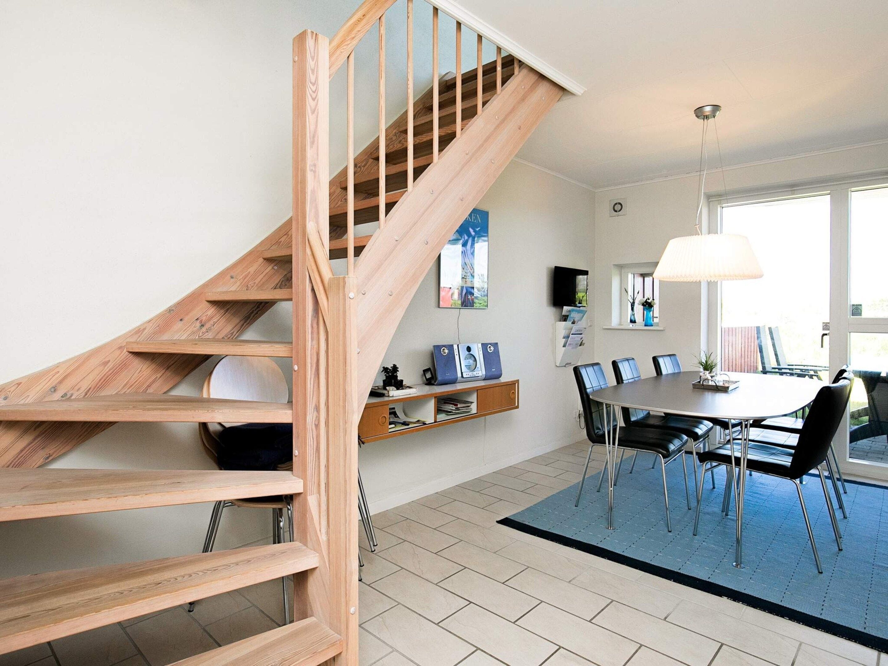 A modern interior with a wooden staircase, a dining area with a table and chairs, and a television mounted on the wall.