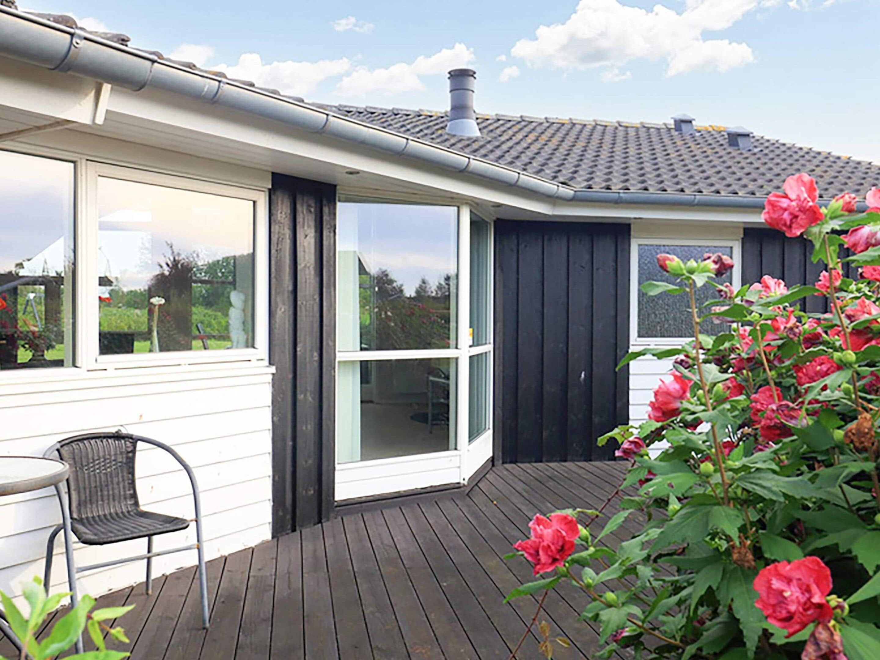 A house with a wooden deck, a black door, and a window overlooking a garden.