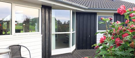 A house with a wooden deck, a black door, and a window overlooking a garden.