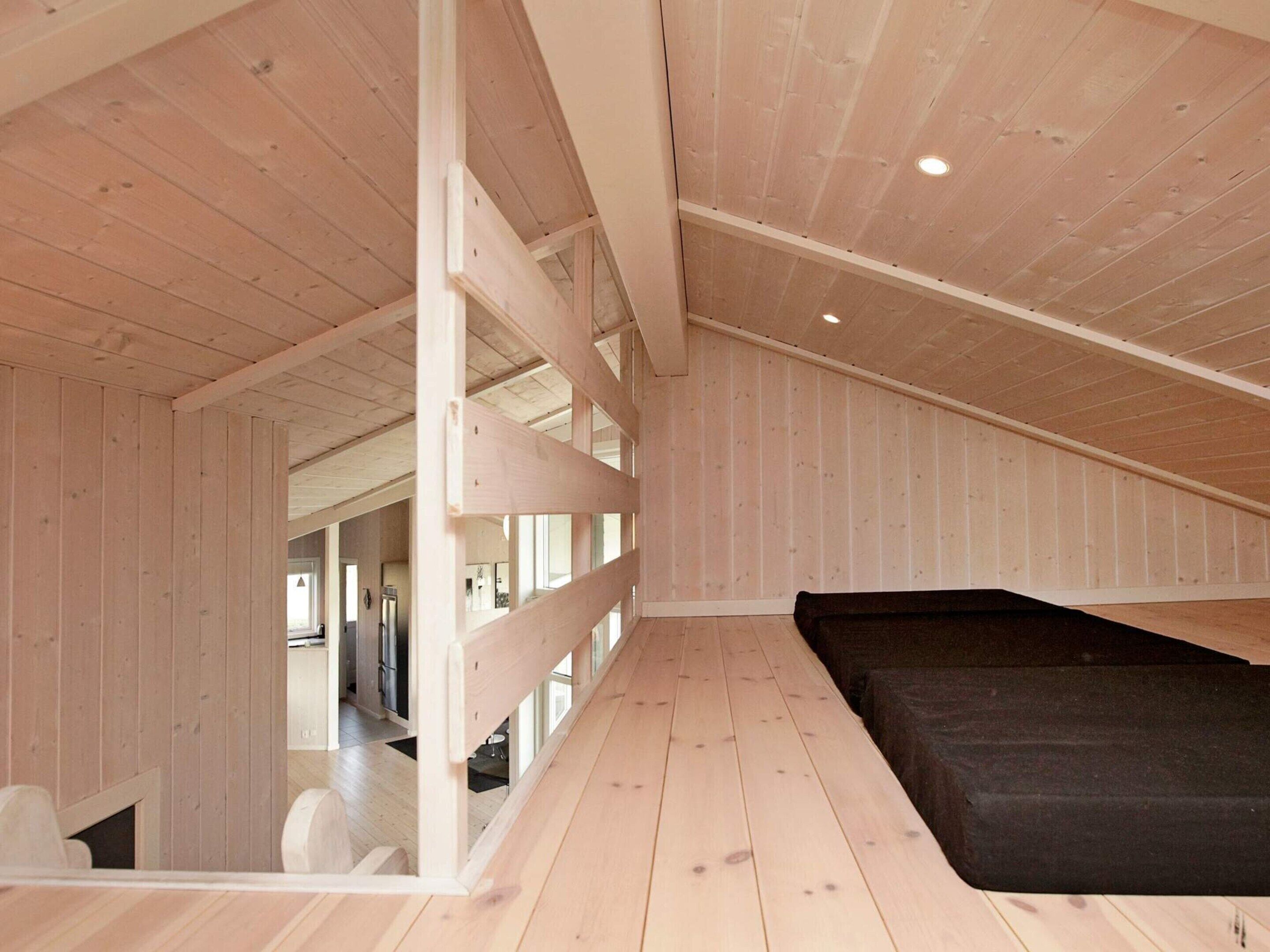 A room with a sloped ceiling, wooden walls, and a black sofa.