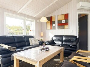 A living room with a black leather sofa, a wooden coffee table, and a black armchair. There is a pendant light above the table and abstract art on the wall.