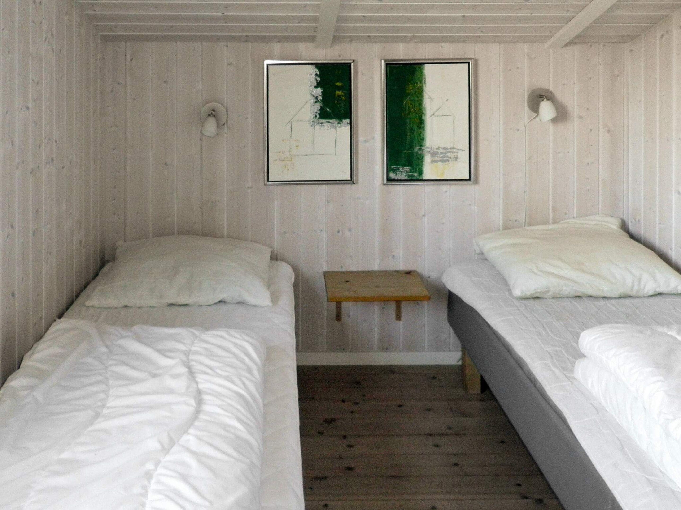 A room with two single beds, a small wooden table, and two framed artworks on the wall.