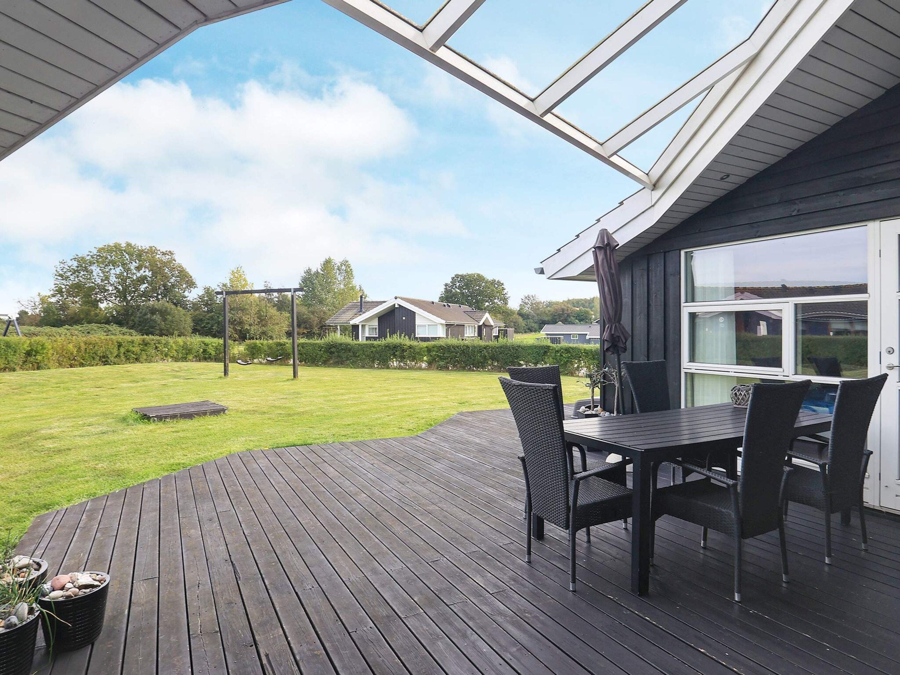 A covered patio with a table and chairs, a wooden deck, and a view of a residential area with houses and greenery.