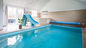An indoor swimming pool with a blue slide, a potted plant, and a view of the outdoors through a glass door. - 5 Star Holiday Home in Tisvildeleje (Vejby)