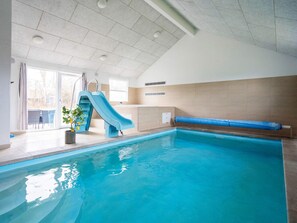 An indoor swimming pool with a blue slide, a potted plant, and a view of the outdoors through a glass door. - 5 Star Holiday Home in Tisvildeleje (Vejby)