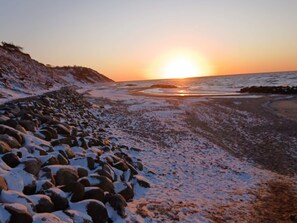 A rocky shoreline with snow-covered rocks and a sunset over the ocean.