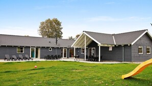 A building with a covered patio area, a grassy lawn, and a yellow slide. - 5 Star Holiday Home in Tisvildeleje (Vejby)