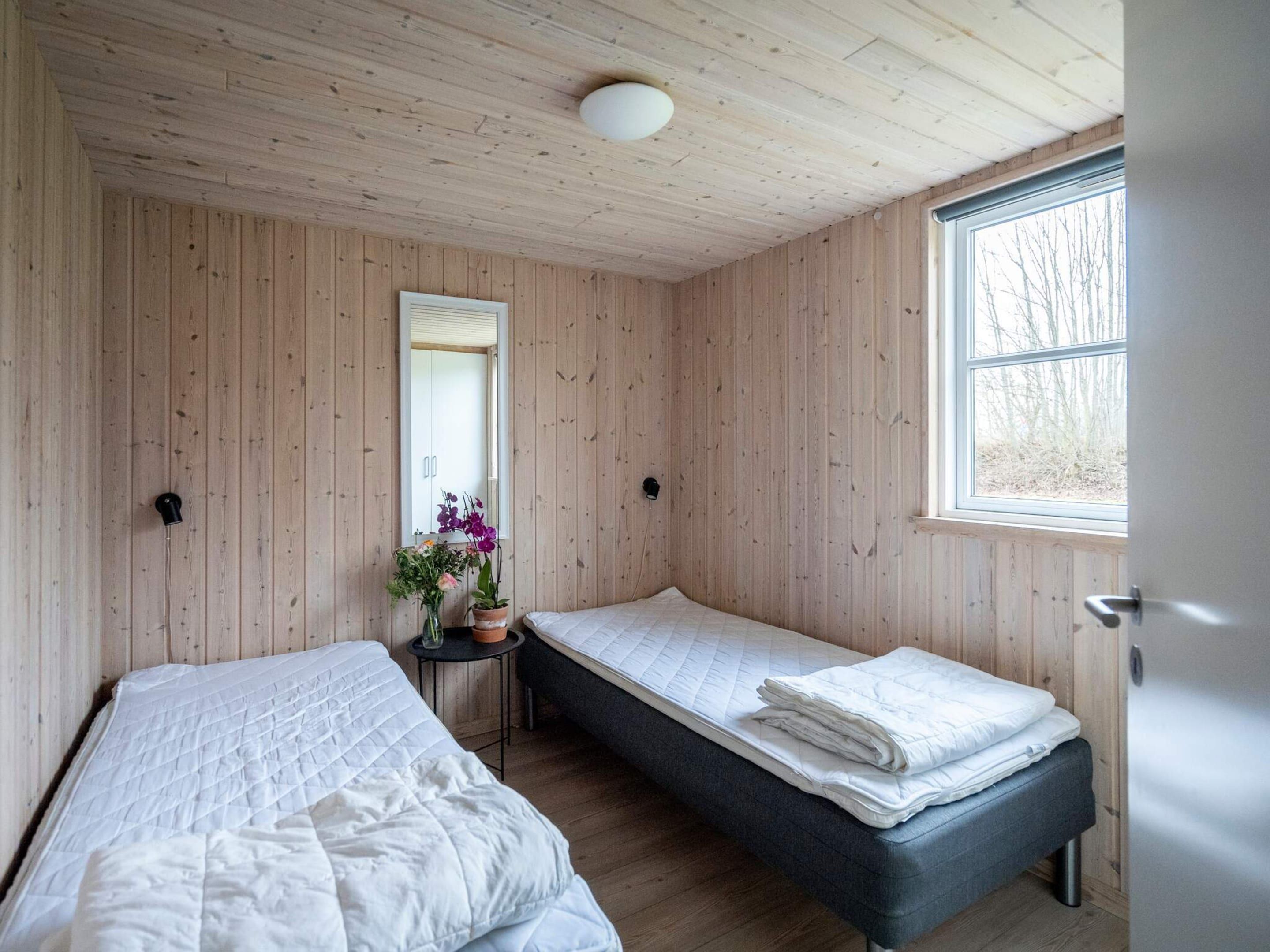 Une chambre avec deux lits, une petite table sur laquelle est posé un vase de fleurs et une fenêtre.