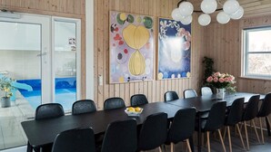 A dining area with a long table, black chairs, and two abstract paintings on the wall.