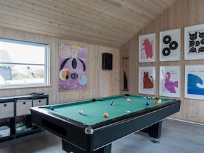 Et poolbord i et rum med trævægge og et vindue. Der er indrammede billeder på væggen, heriblandt et med en kat og et med en bølge.