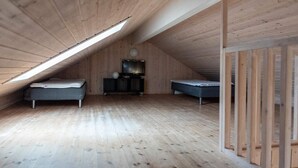 A high-ceilinged attic room with wooden walls and floors, featuring two beds, a TV, and a small cabinet.