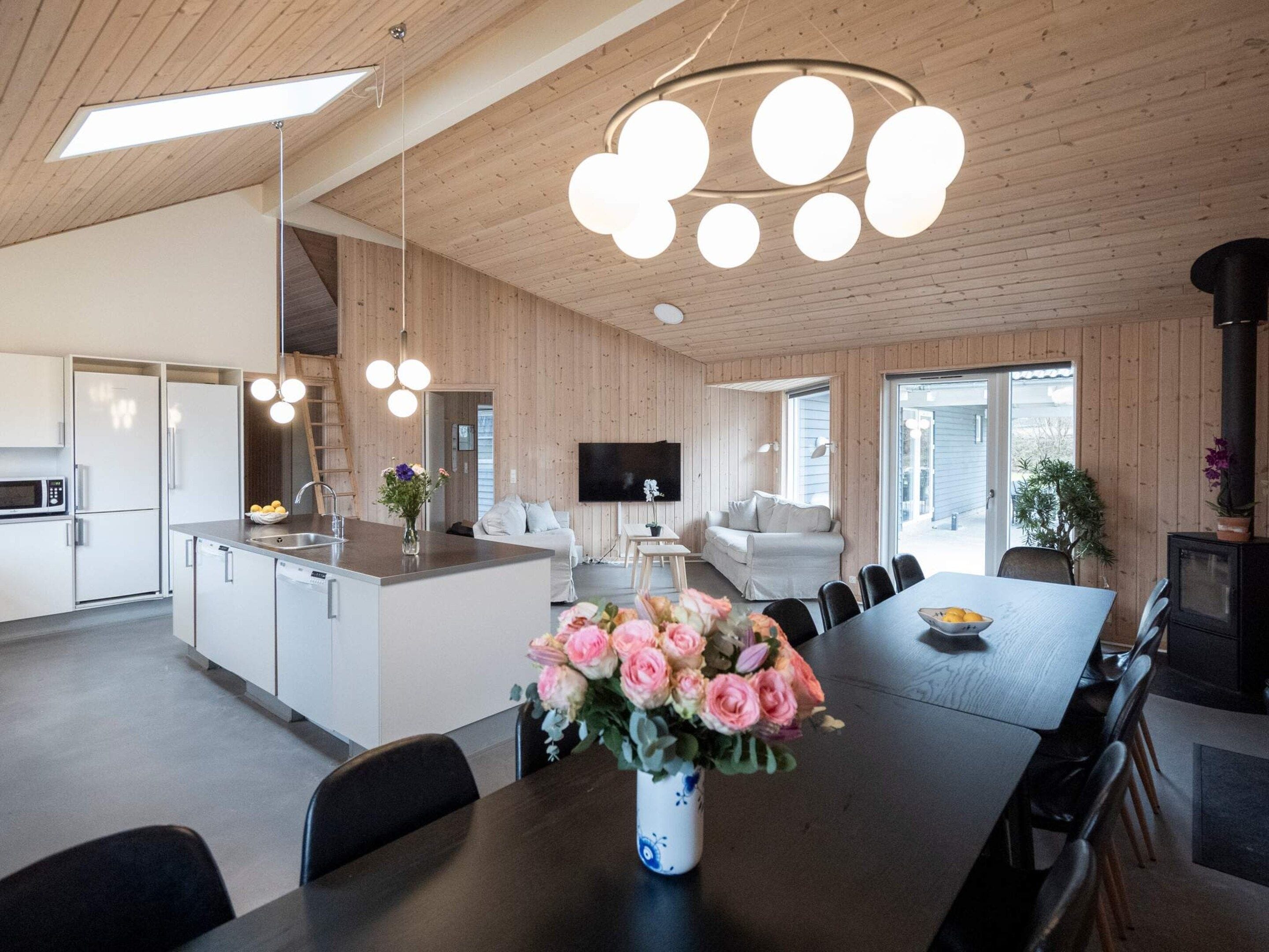 A modern kitchen with a central island, a dining area with a long table, and a living space with a sofa and TV.