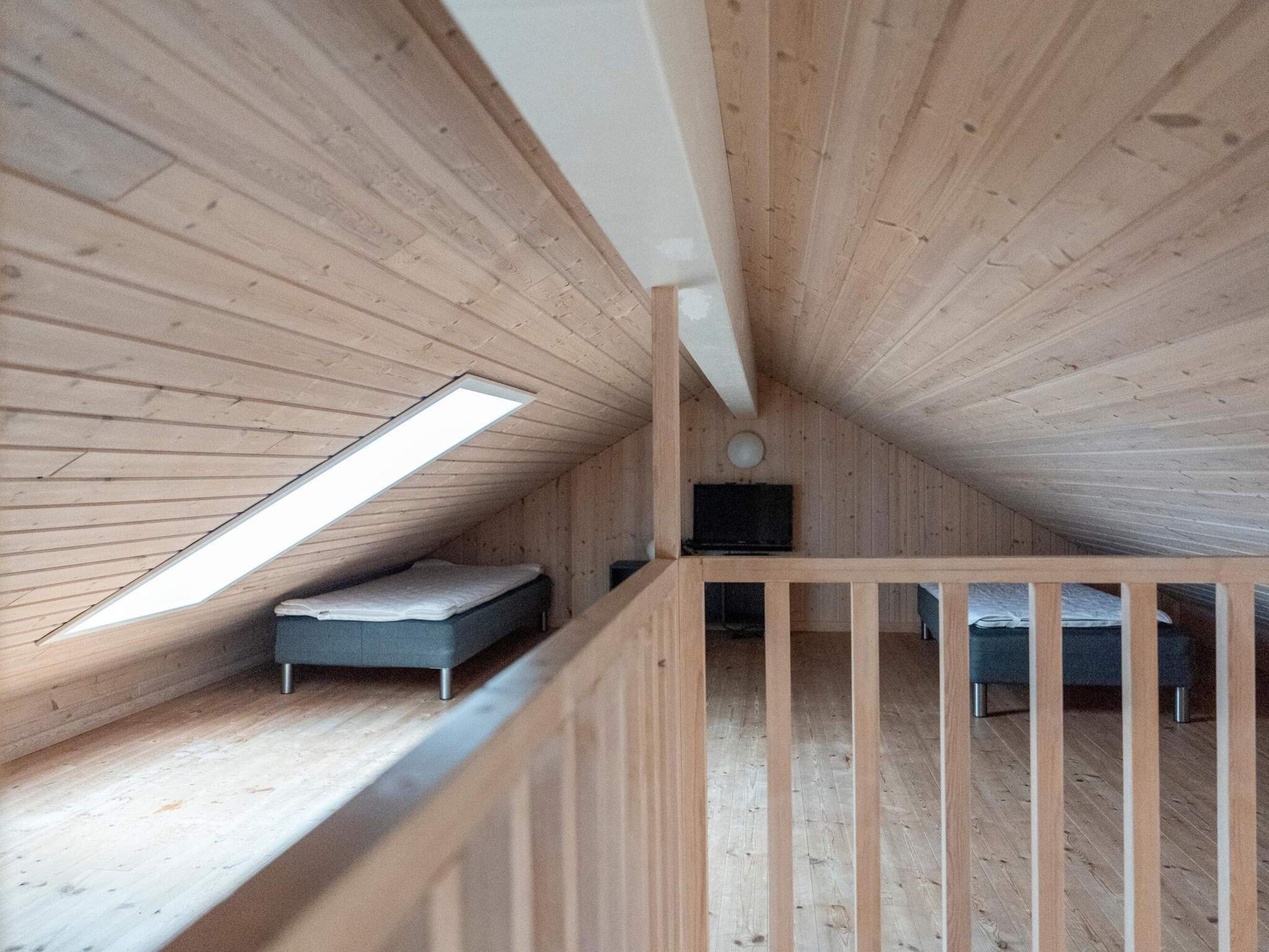 Une chambre mansardée en bois, avec une lucarne, un lit et un téléviseur.