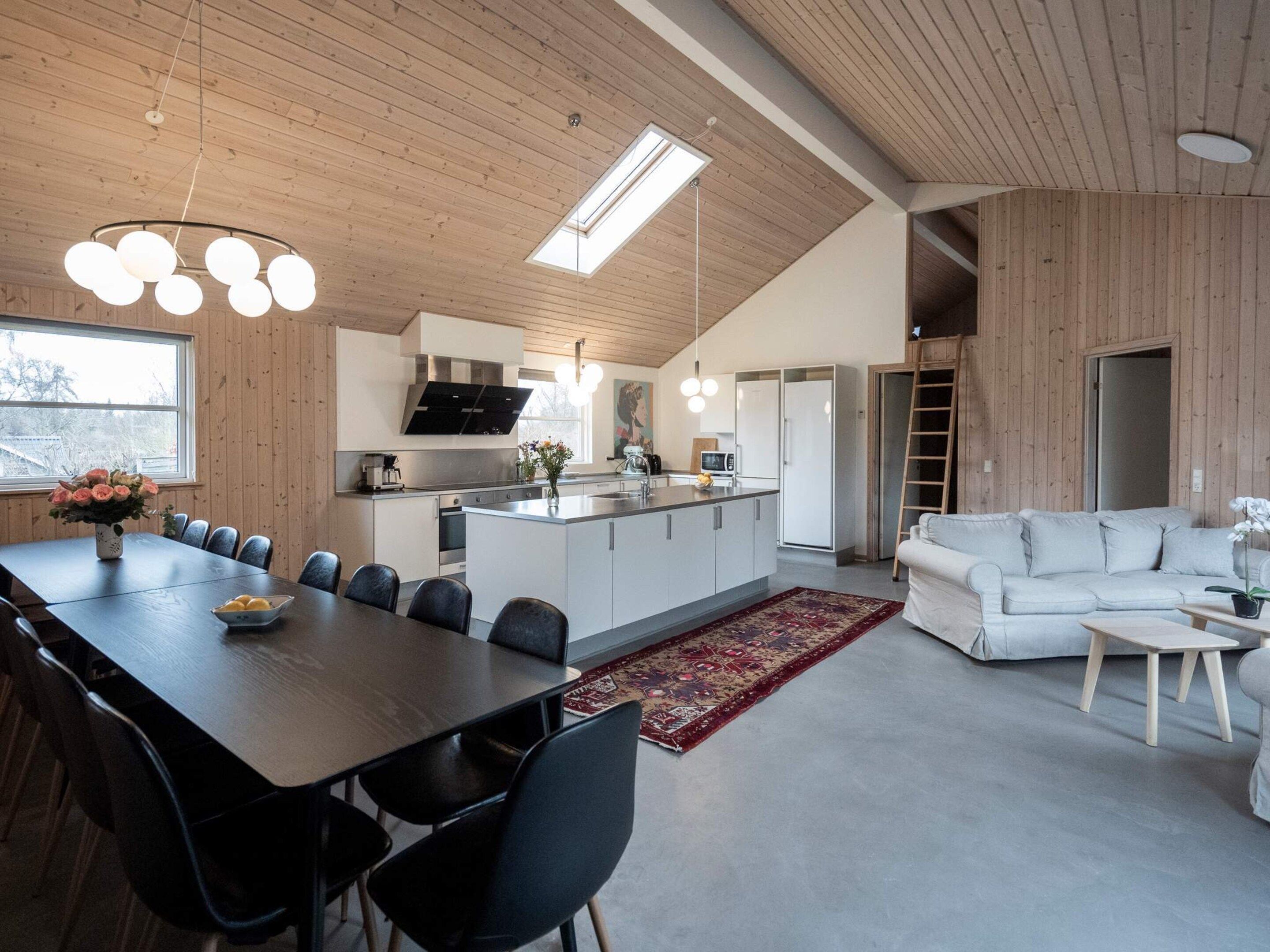 A modern kitchen with a central island, a dining area with a long table and chairs, and a living area with a sofa and coffee table.