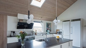 A modern kitchen with a central island, white cabinetry, a large window, and a skylight.