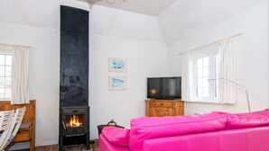 A cozy living room with a fireplace, a pink sofa, a television, and a dining area with chairs and a table. - Serene Holiday Home in Fanø near Restaurants (Fano)