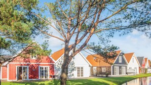 Una hilera de casas tradicionales con fachadas rojas y blancas, un césped y una masa de agua tranquila.