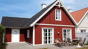 Una casa roja y blanca con techo negro, puerta principal y patio con mobiliario exterior.