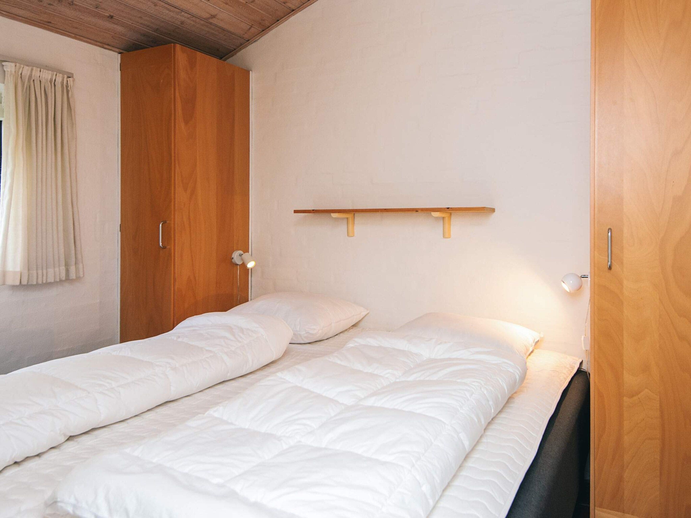 Una cama individual con cabecera de madera, una mesita de noche y un estante fijado a la pared.