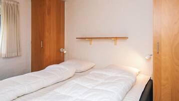 Una cama individual con cabecera de madera, una mesita de noche y un estante fijado a la pared.