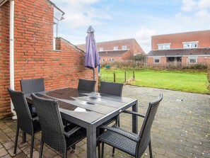 A patio with a glass table and four wicker chairs, a purple umbrella, and a brick wall. - 4 Star Holiday Home in Blavand (Blavand)